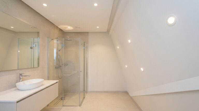 Salle de bain lumineuse avec spots LED encastrés au plafond et dans le mur incliné au-dessus de la douche.